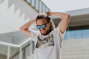 Smiling man in blue sunglasses and matching blue sunblock on nose. fixing his hair